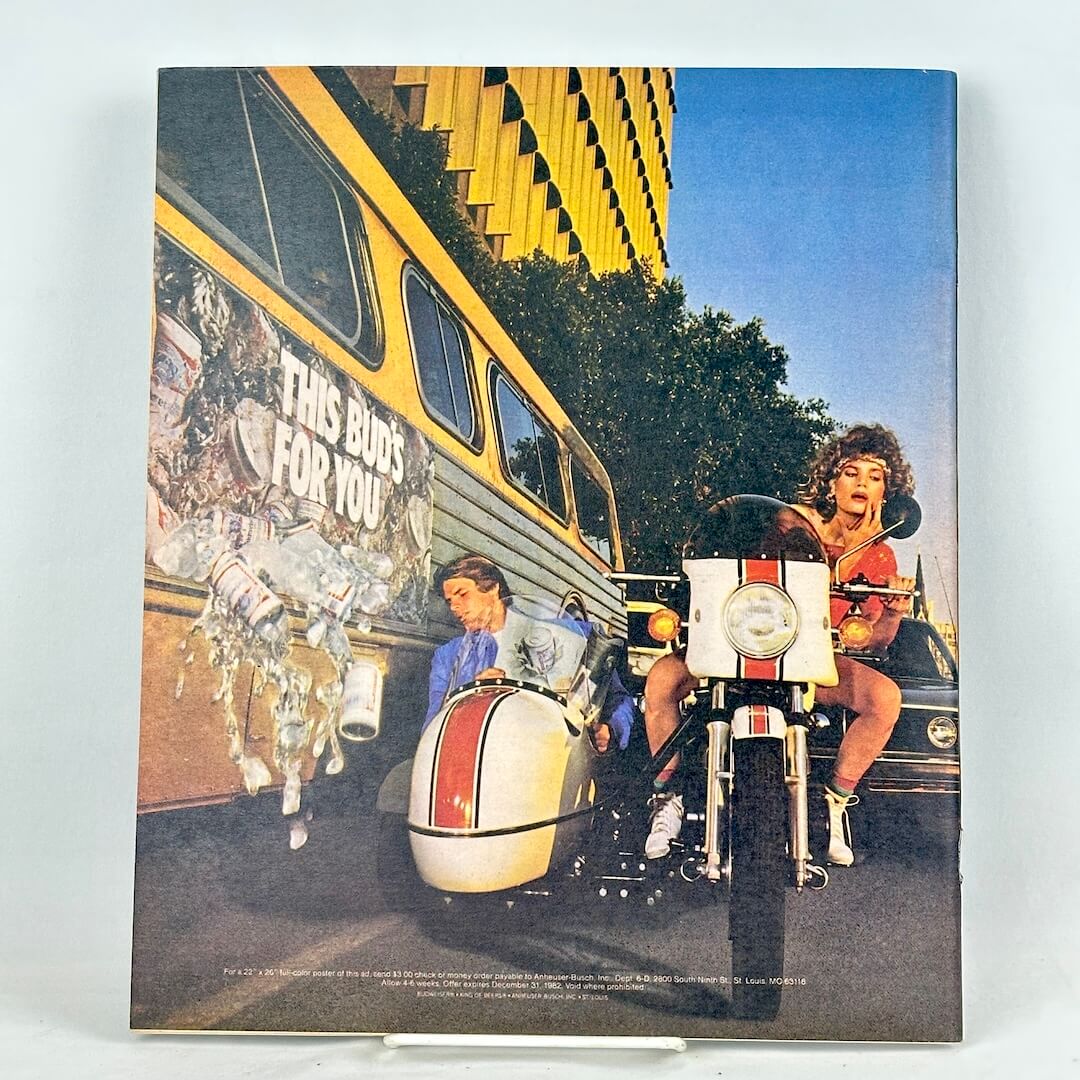 Back cover of magazine showing an ad with woman riding a white motorcycle with a sidecar next to a yellow bus.