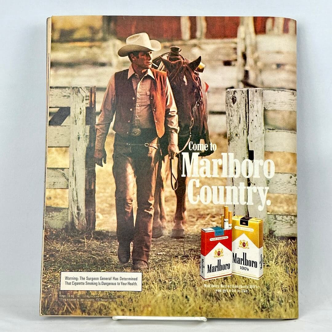 Back cover of magazine with full page ad for Marlboro cigarettes featuring a cowboy leading a horse through fence.