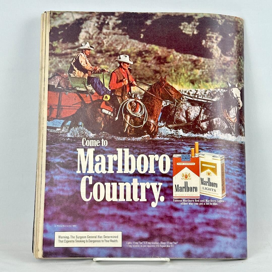 Back cover of magazine with full page ad for Marlboro cigarettes featuring two mounted cowboys wading through water.