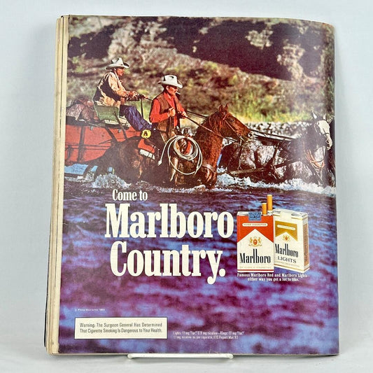 Back cover of magazine with full page ad for Marlboro cigarettes featuring two mounted cowboys wading through water.