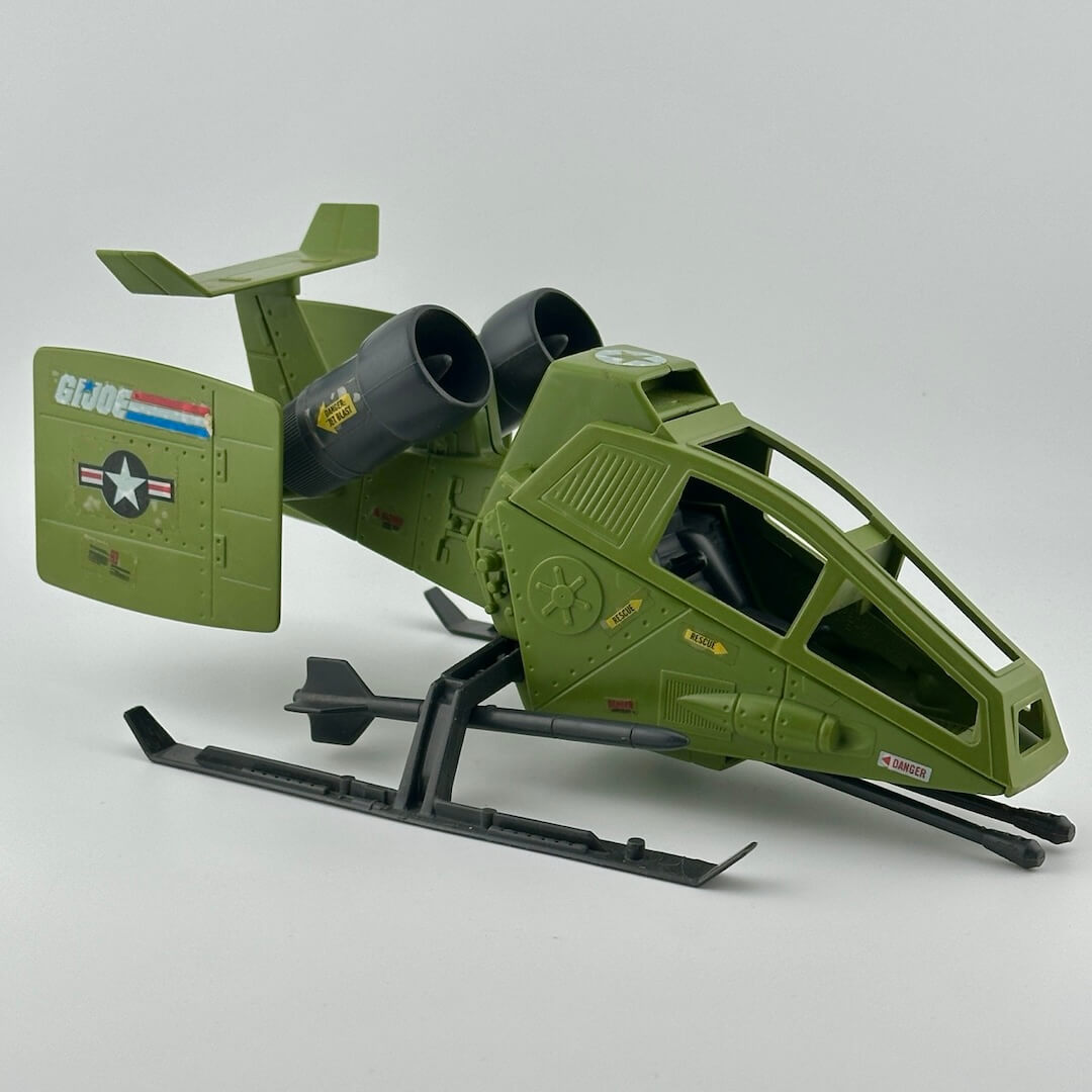 Army green helicopter with twin grey engines, two grey missiles on landing gear, gun at front, & G.I. Joe sticker decals