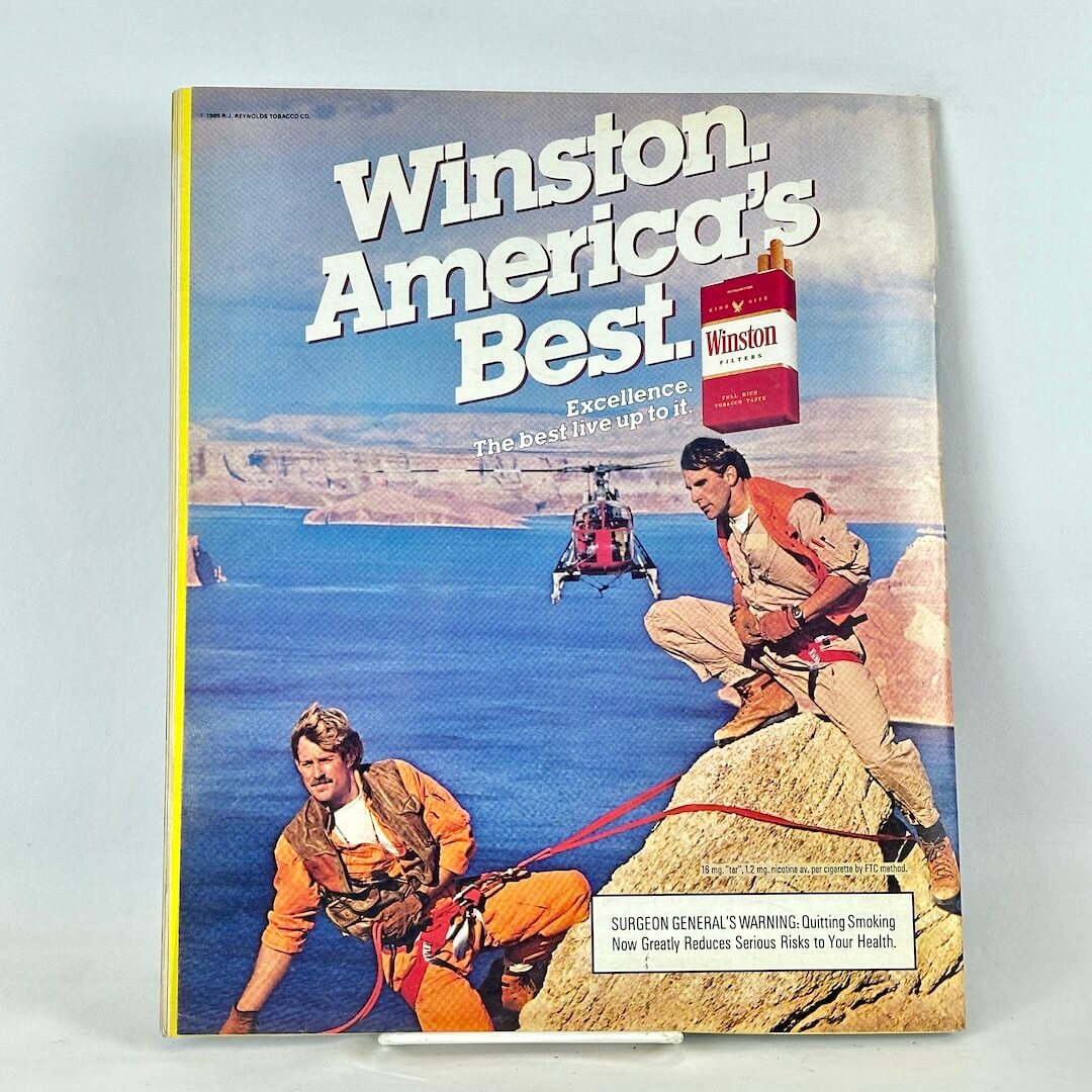Back cover of magazine with full page ad for Winston cigarettes with outdoors scene and two men pictured.
