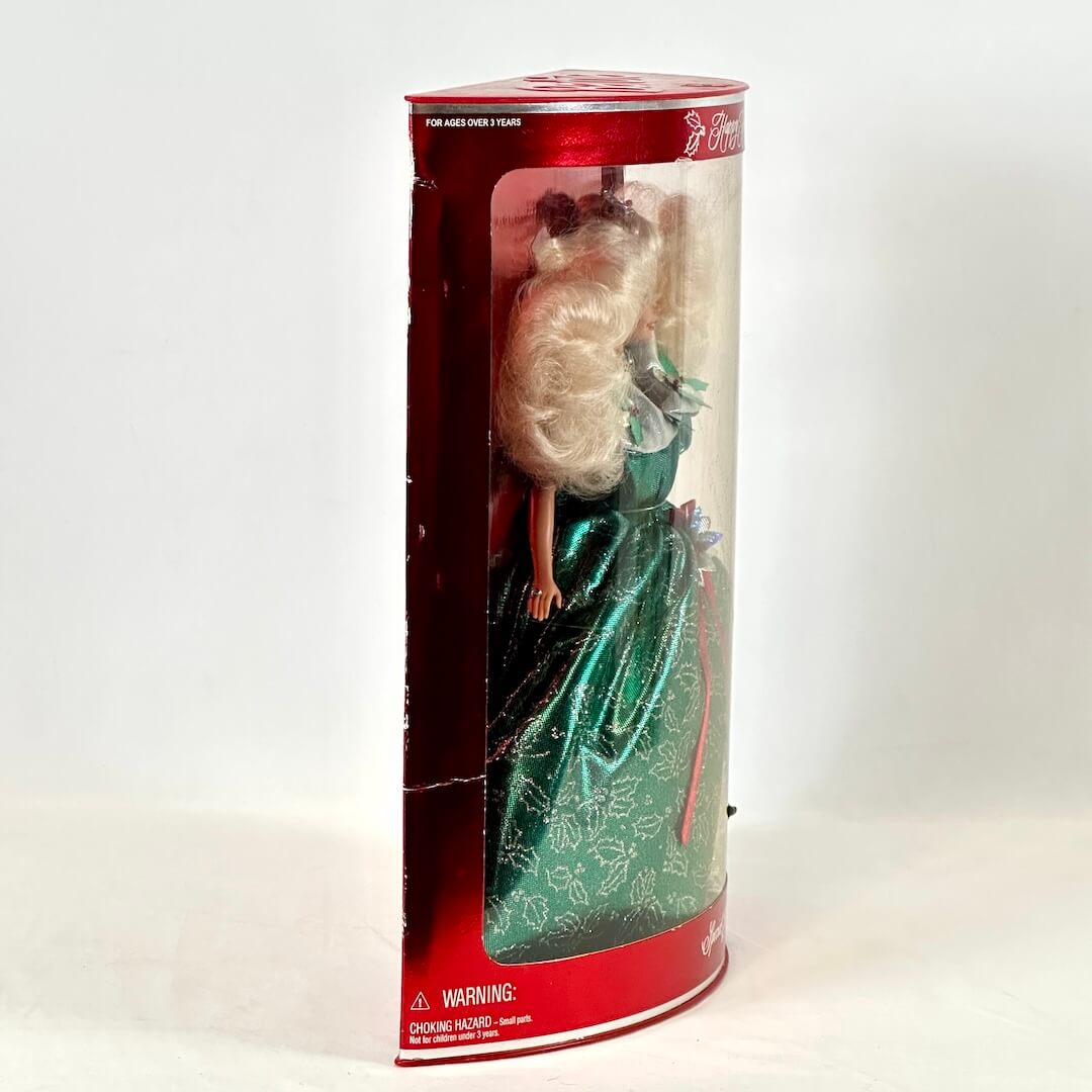 Barbie doll in a green dress inside a cylindrical packaging with a red top on a white background