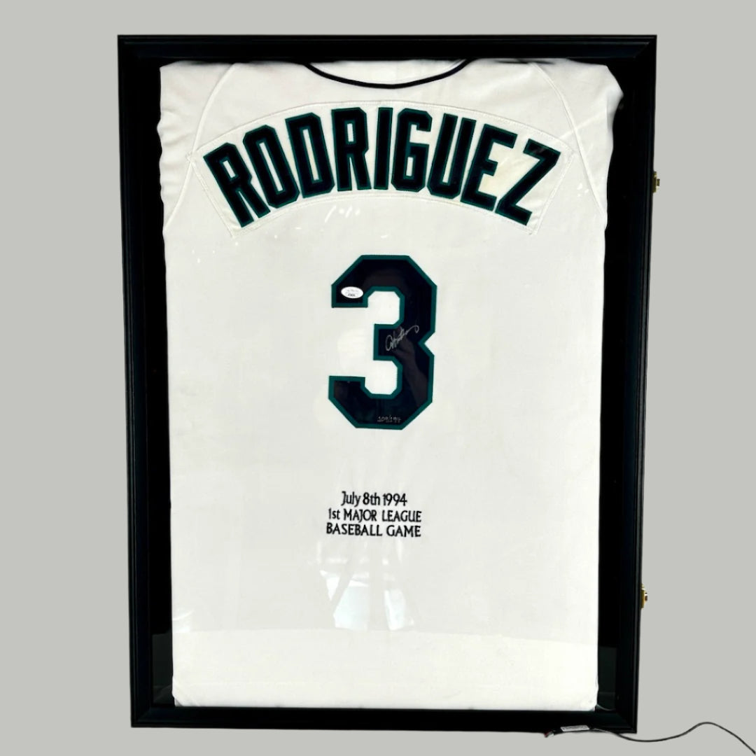 Black jersey frame containing white baseball jersey with dark navy letters with dark teal shadow effect, signed by player.