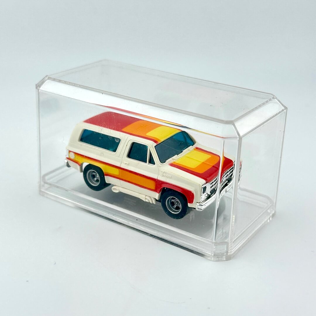 Model of a vintage Blazer with a colorful design inside a clear display case on a light gray background