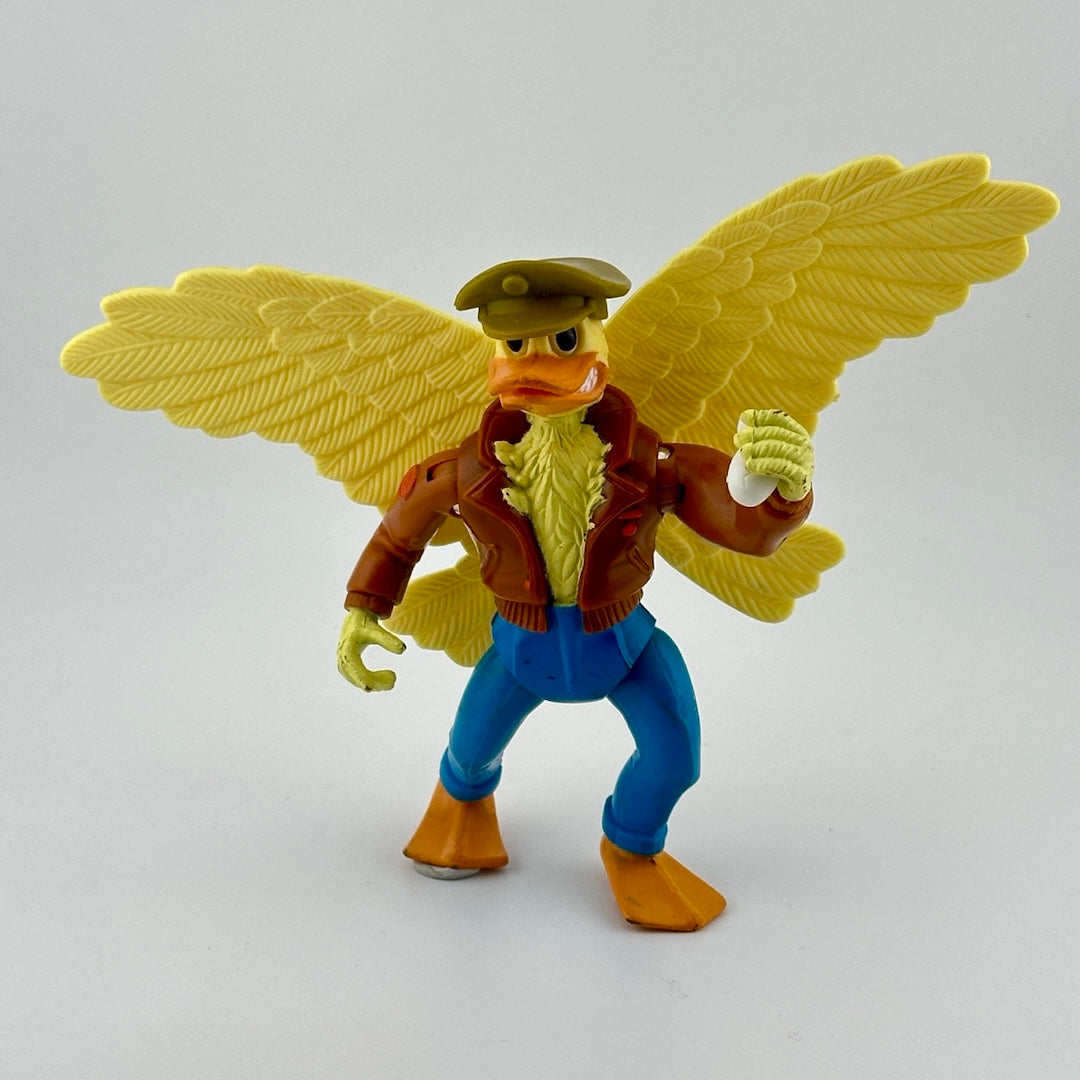 Yellow anthropomorphic bird in jeans, leather bomber jacket, & military cap. Holding white grenade. Front view.