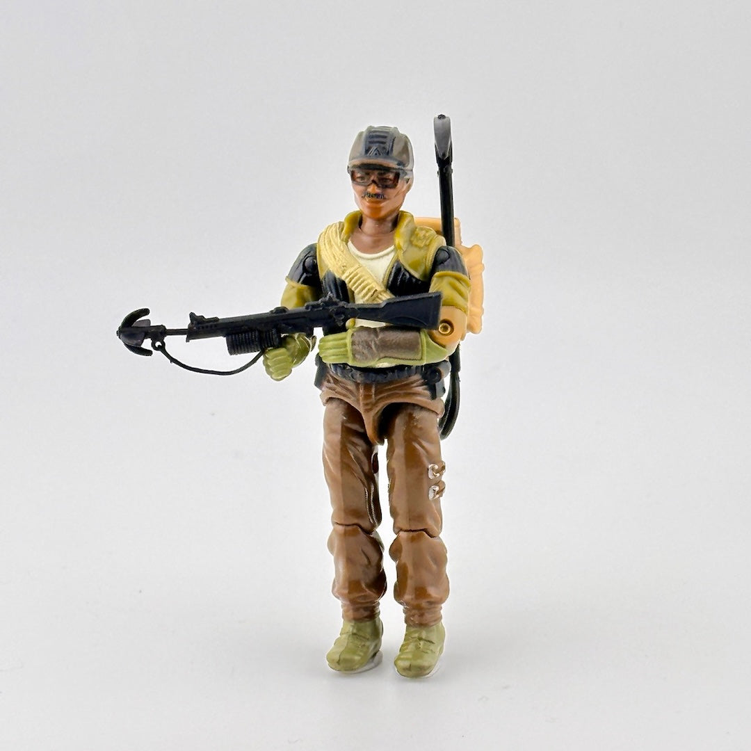 Male action figure in brown pants, camo shirt, brown helmet, with black grappling gun, pick, shovel, & beige backpack.
