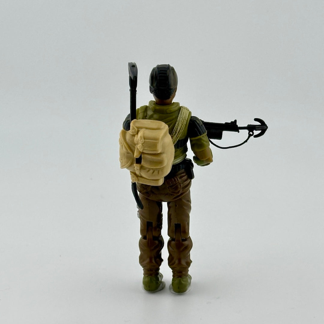 Male action figure in brown pants, camo shirt, brown helmet, with black grappling gun, pick, shovel, & beige backpack.