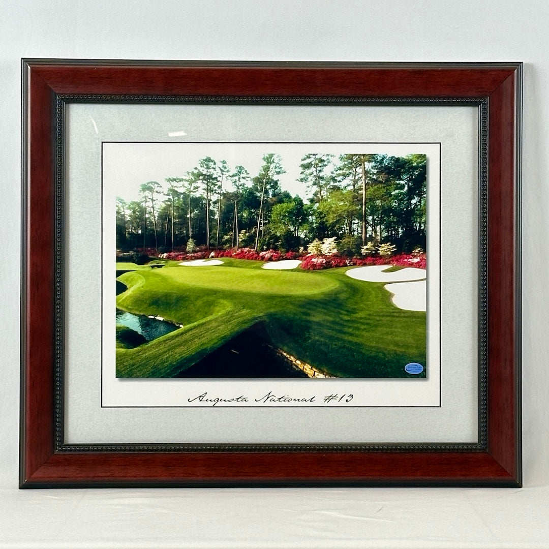 Brown framed and white matted photo of golf course hole with trees and flowers in background.
