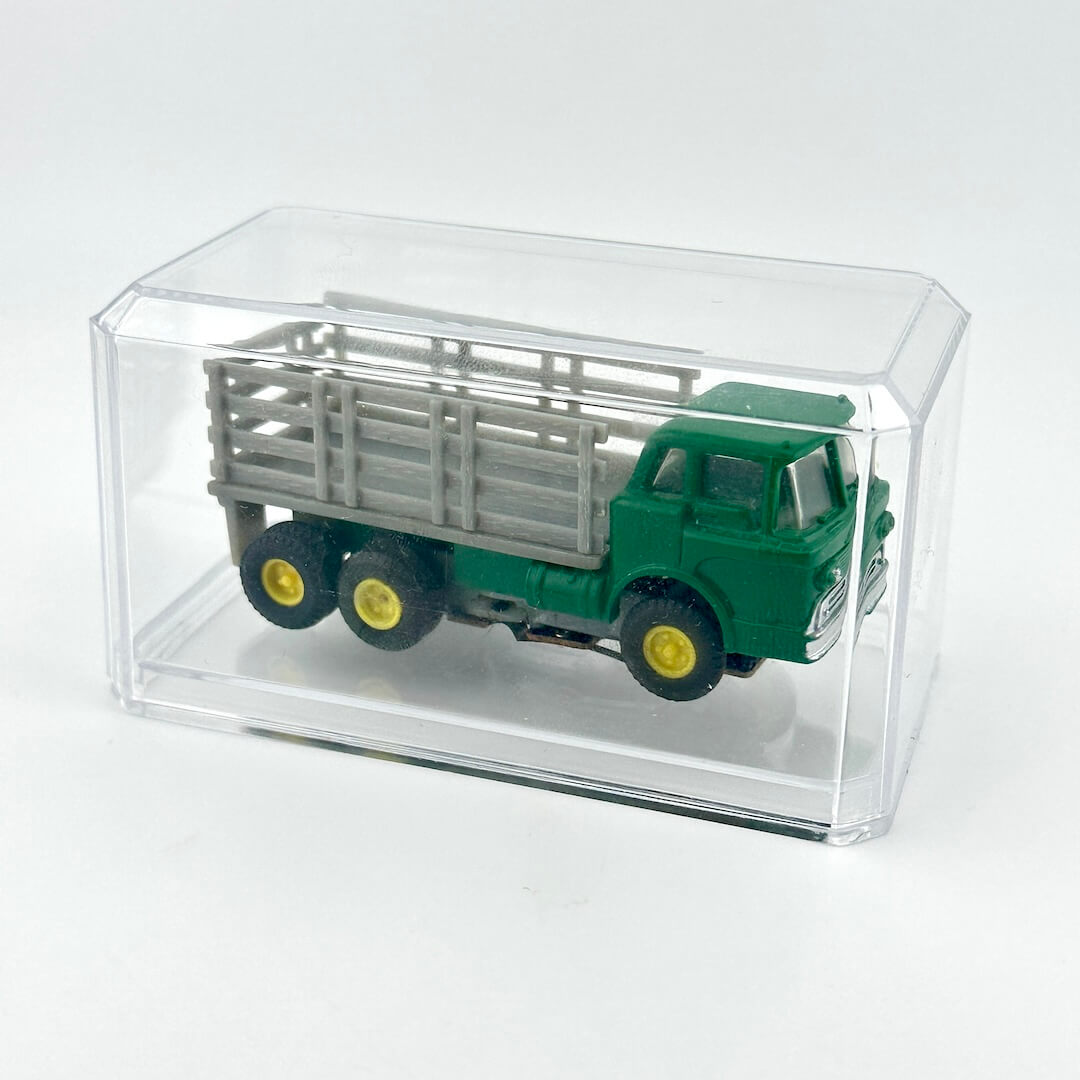 Green toy truck with a silver trailer inside a clear display case on a white background