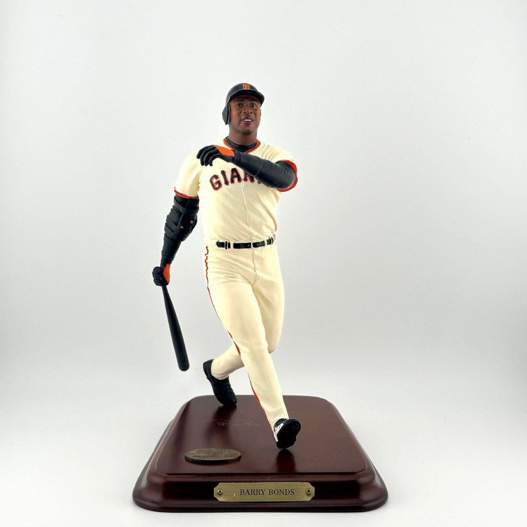 Baseball player in white Giants uniform with bat at the end of a swing on a wooden base with gold plaques.