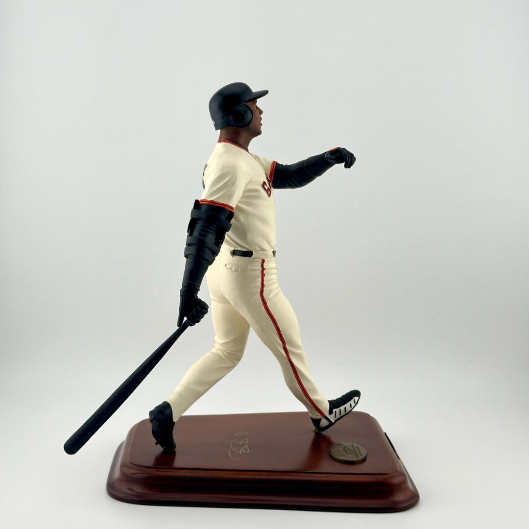 Baseball player in white Giants uniform with bat at the end of a swing on a wooden base with gold plaques.