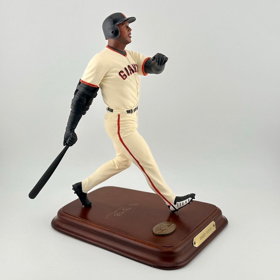 Baseball player in white Giants uniform with bat at the end of a swing on a wooden base with gold plaques.