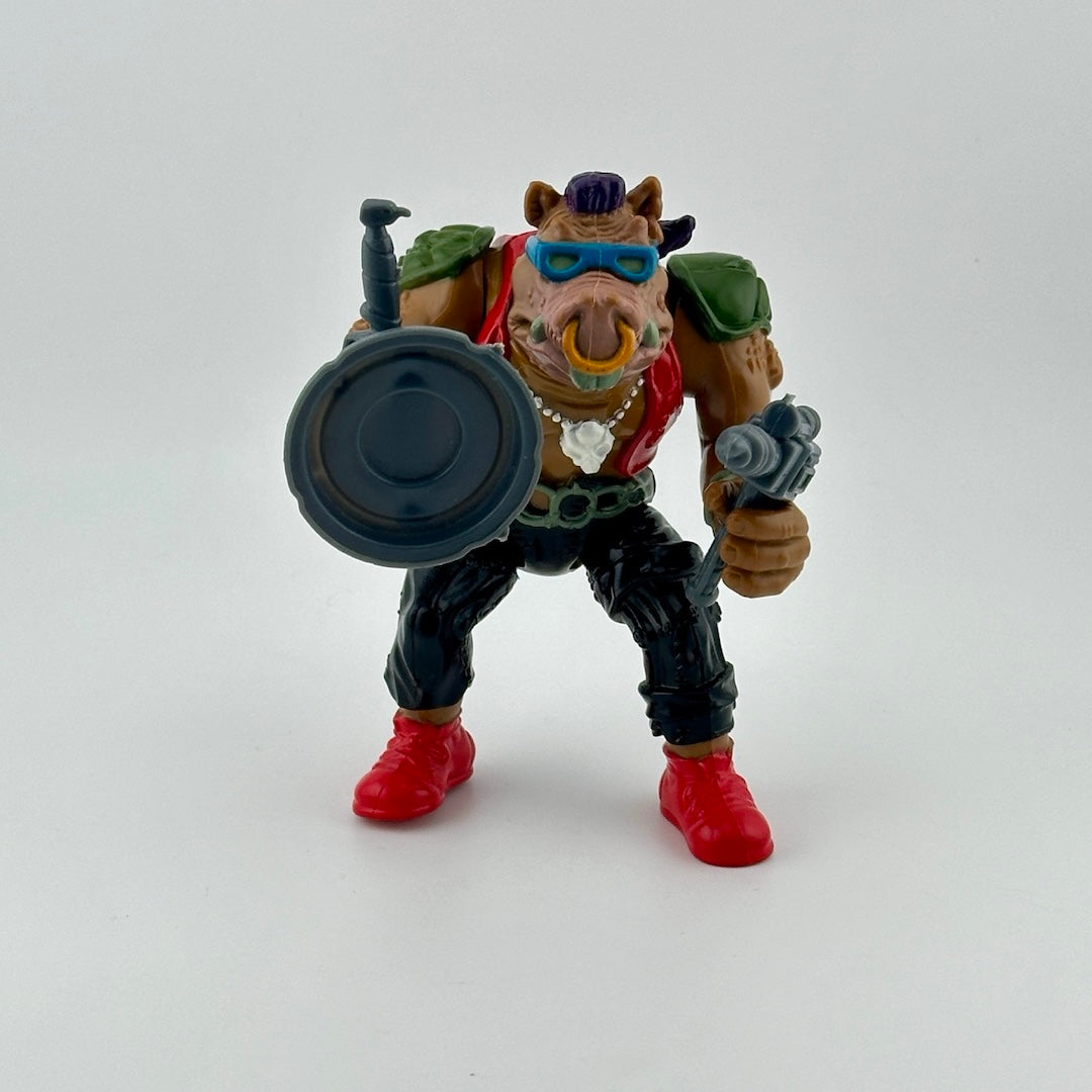 Anthropomorphic hog in pants, vest, with nosering & armor, holding gun, knife & sewer lid shield. Front.