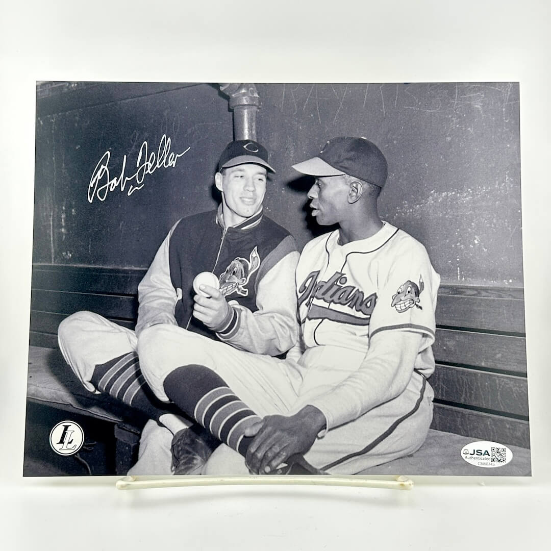 Two baseball players sitting on a bench with a signature above them, framed by a white border.