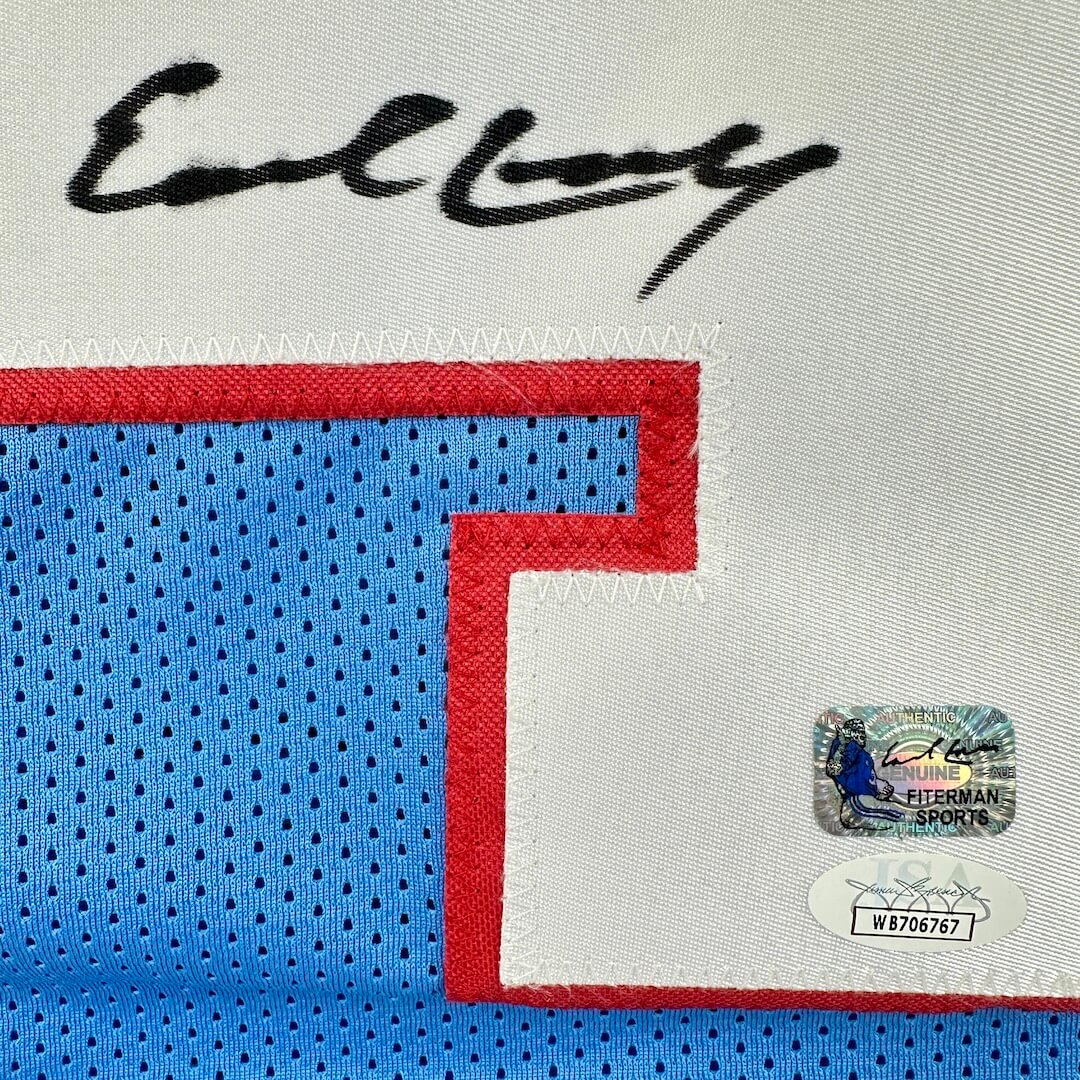 Close-up of a sports jersey with a signature, & two authentication stickers on stitched on letter.