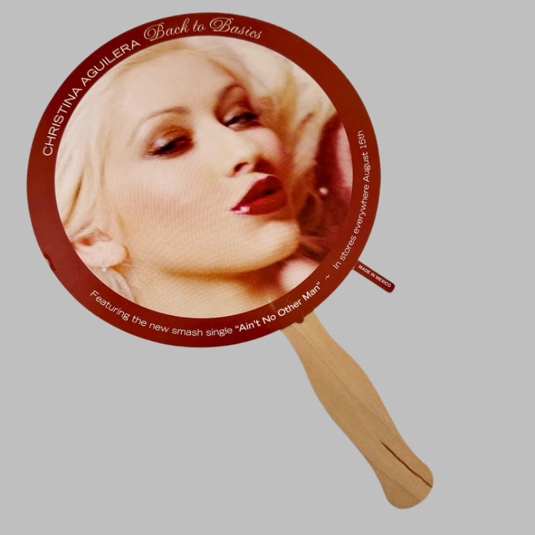 Circular fan with wooden handle. Main image of artist pursing lips & looking into camera, with red border with album info.