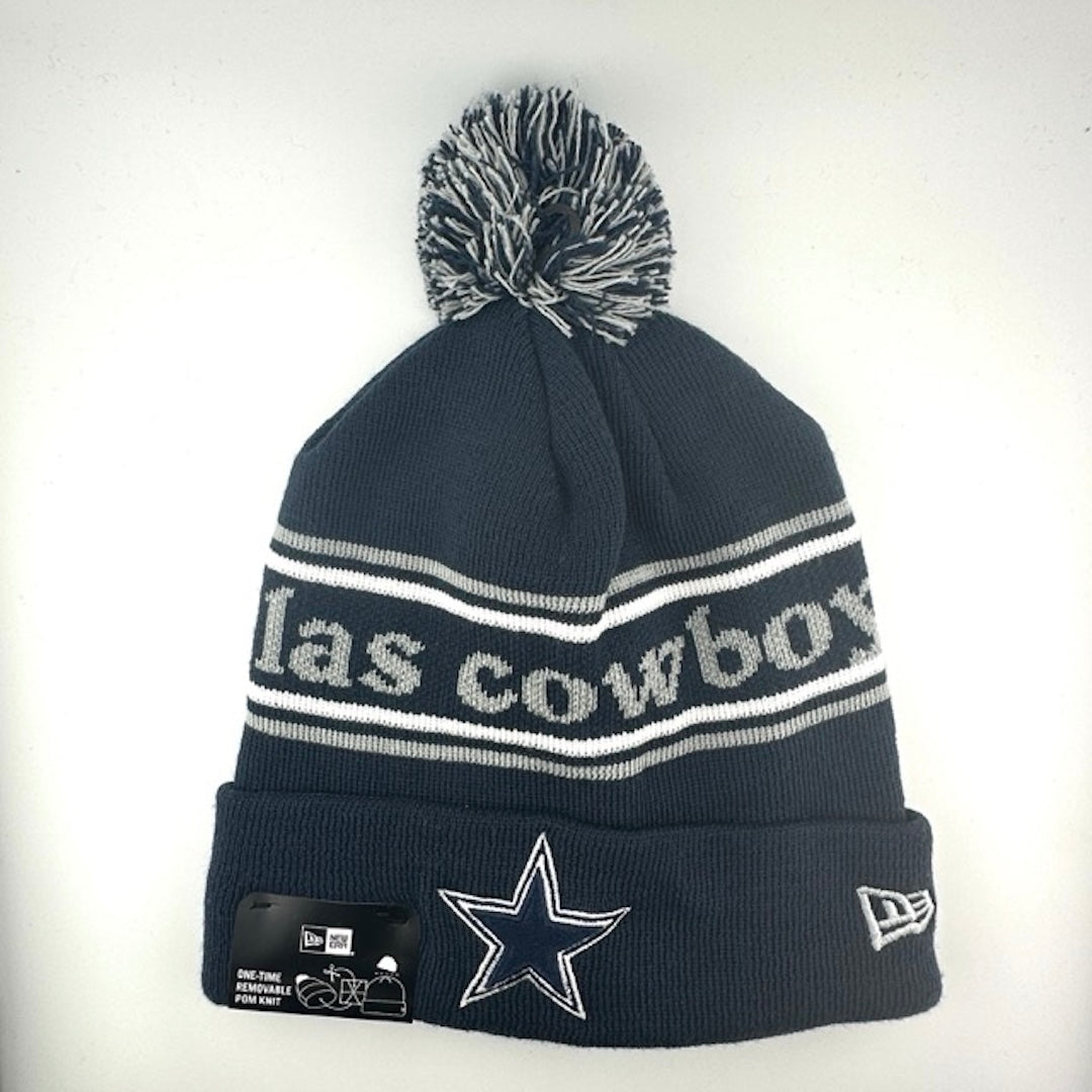 Navy knit hat with white/grey stripes around center banner featuring grey text. White/grey/navy pom at top. Star logo center.