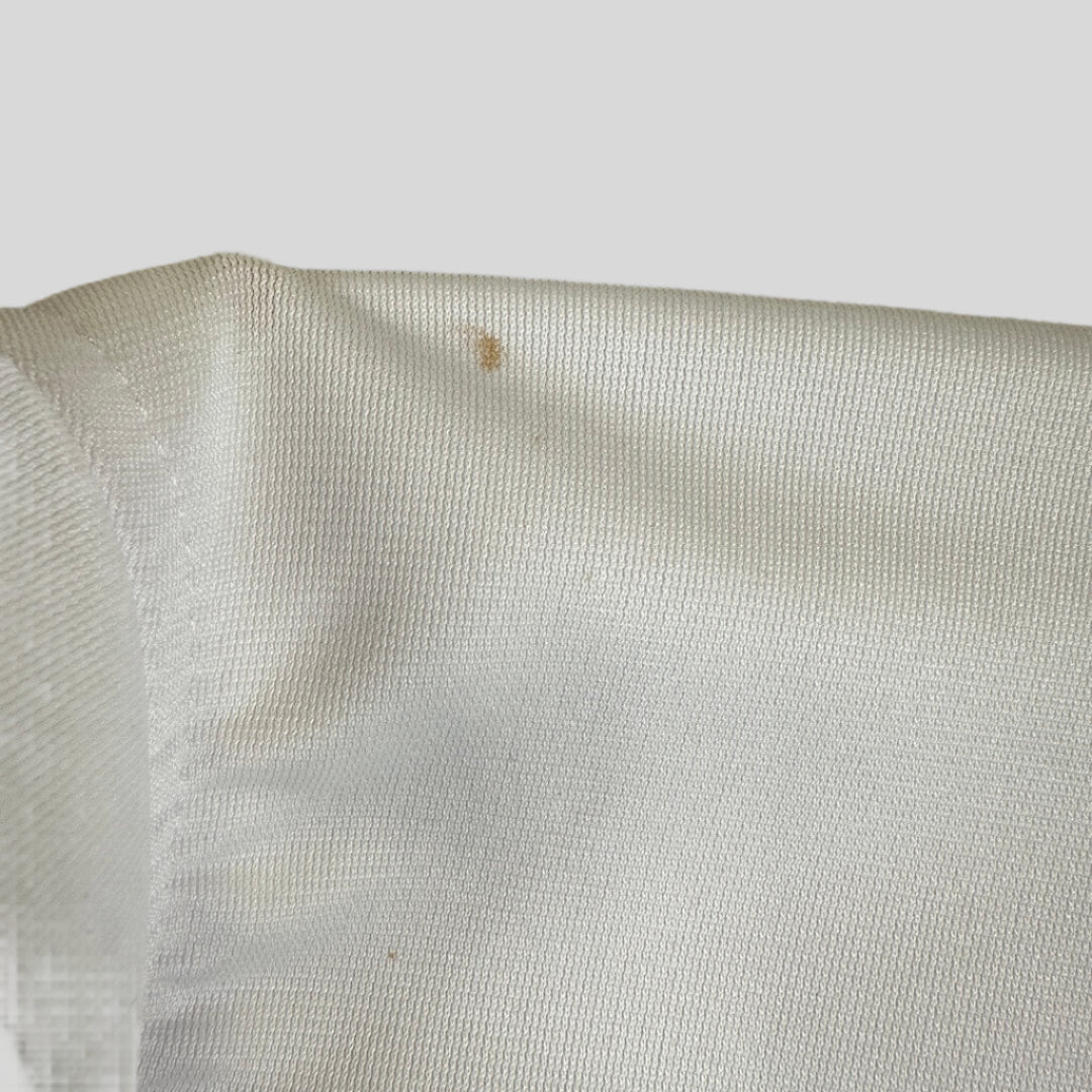 Close-up of a white fabric with a small brown stain on a light background