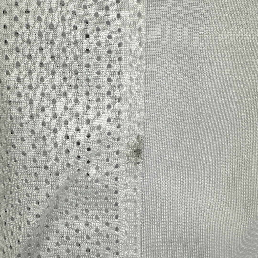Close-up of a gray fabric with a mesh pattern and small black smudge on seam.