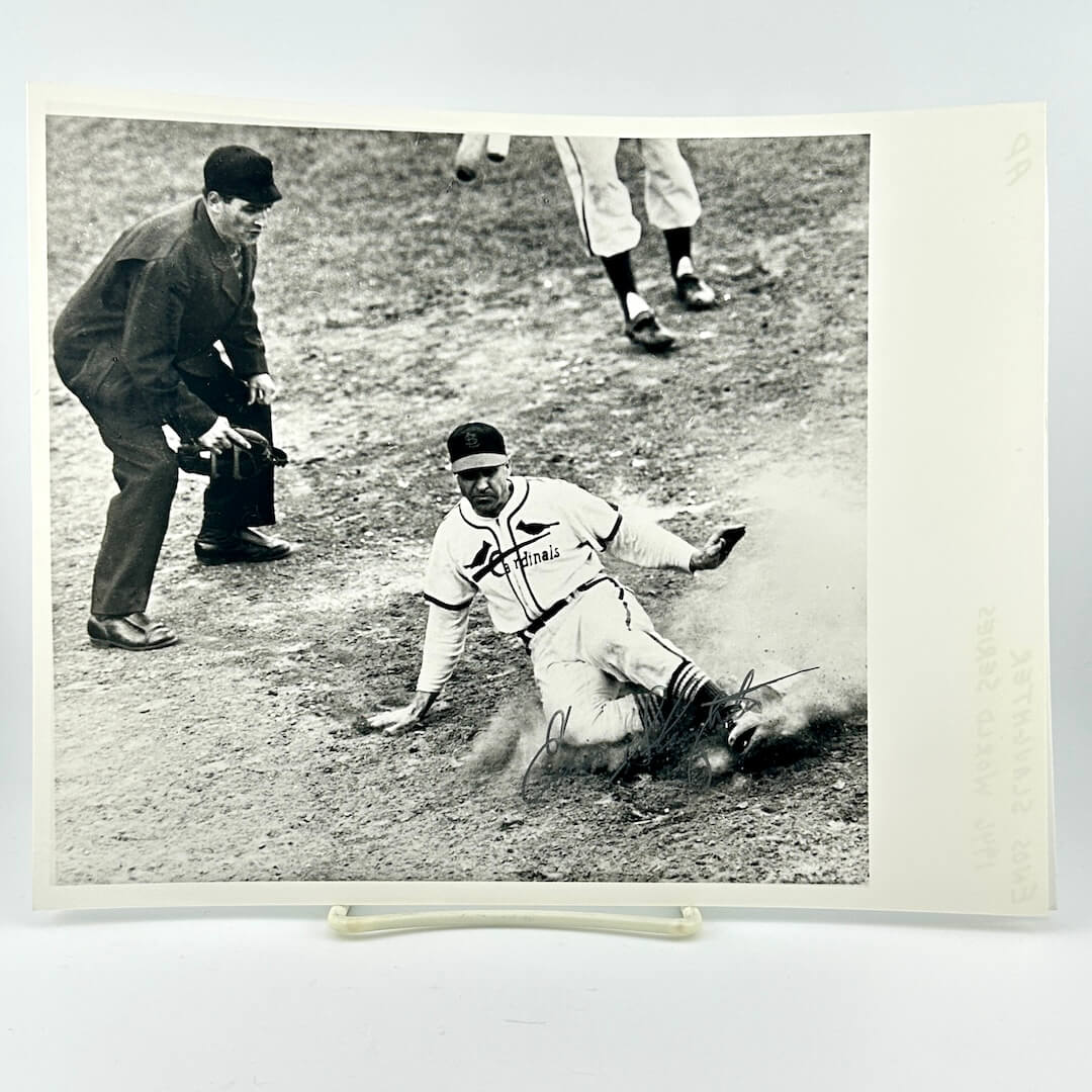 Vintage black and white photograph of a baseball player sliding into home plate with an umpire and another player in the background.