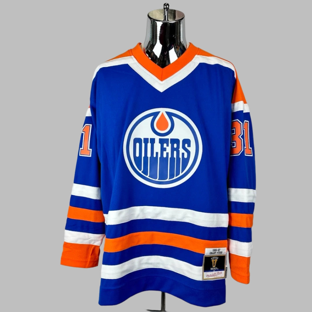Jersey blue body & long sleeves, orange shoulders, white/orange stripes around waist & wrists. OILERS logo center chest.