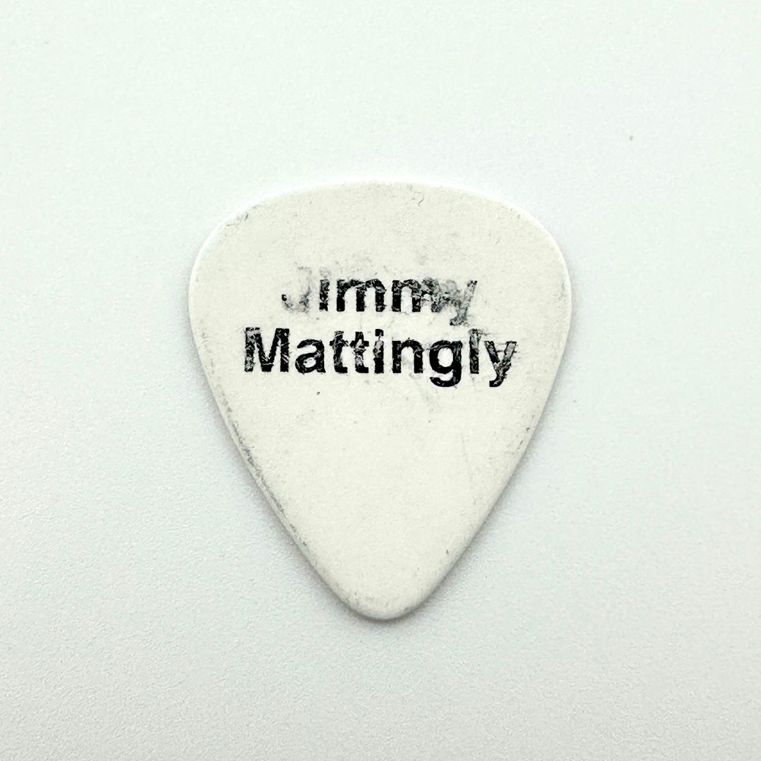 A white guitar pick printed with the black text 'Jimmy Mattingly' on a light gray background.