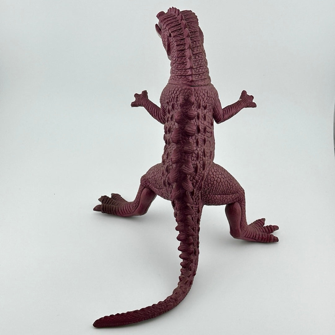 Back of purple dinosaur type animal with white tusks & teeth, black eyes. Ridges all down back.