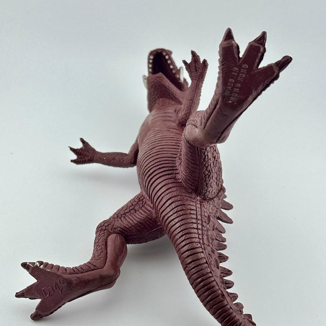 Underside of purple dinosaur type animal with white tusks & teeth, black eyes, showing manufacturer info.