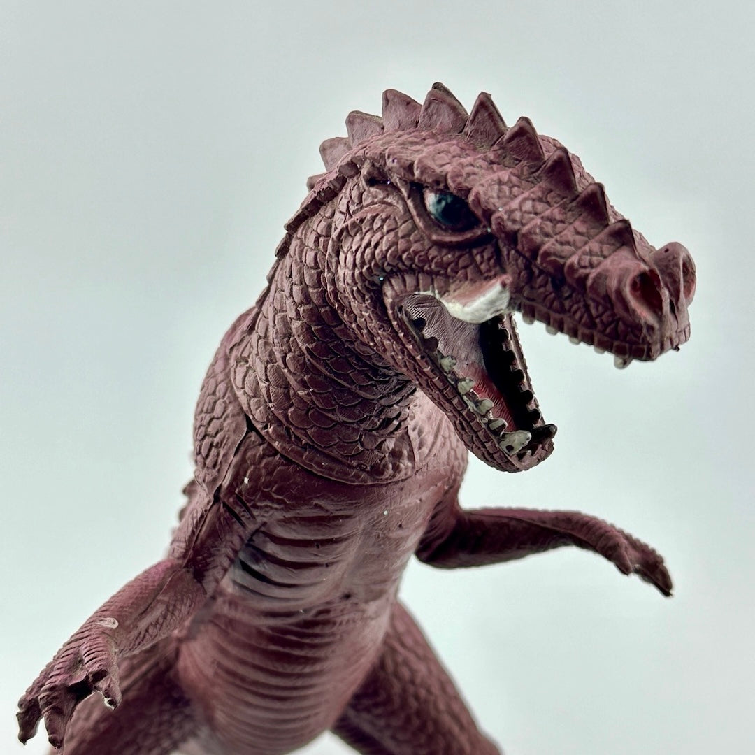 Close up of purple dinosaur type animal with white tusks & teeth, black eyes.