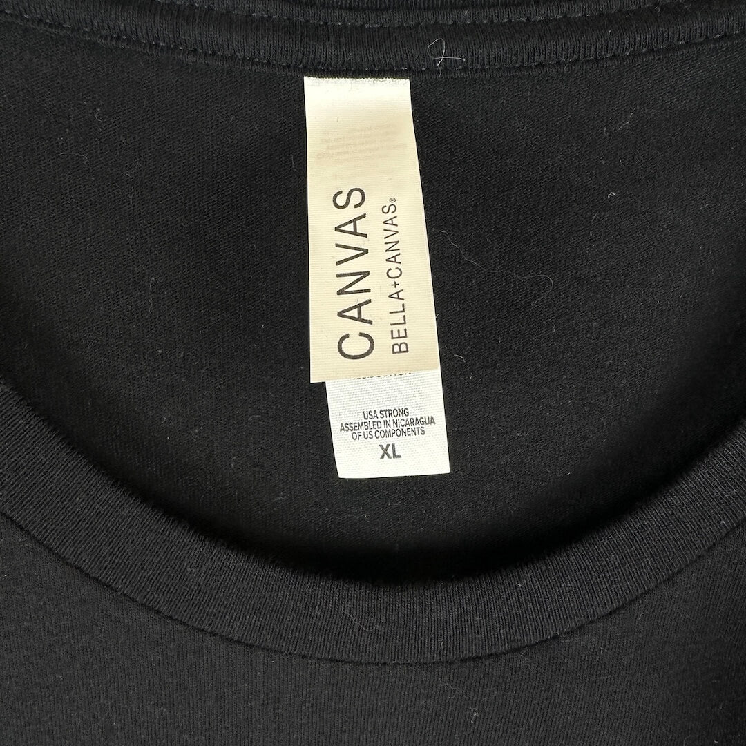 Close-up of a black Bella+Canvas crewneck shirt showing the neck label with size XL.