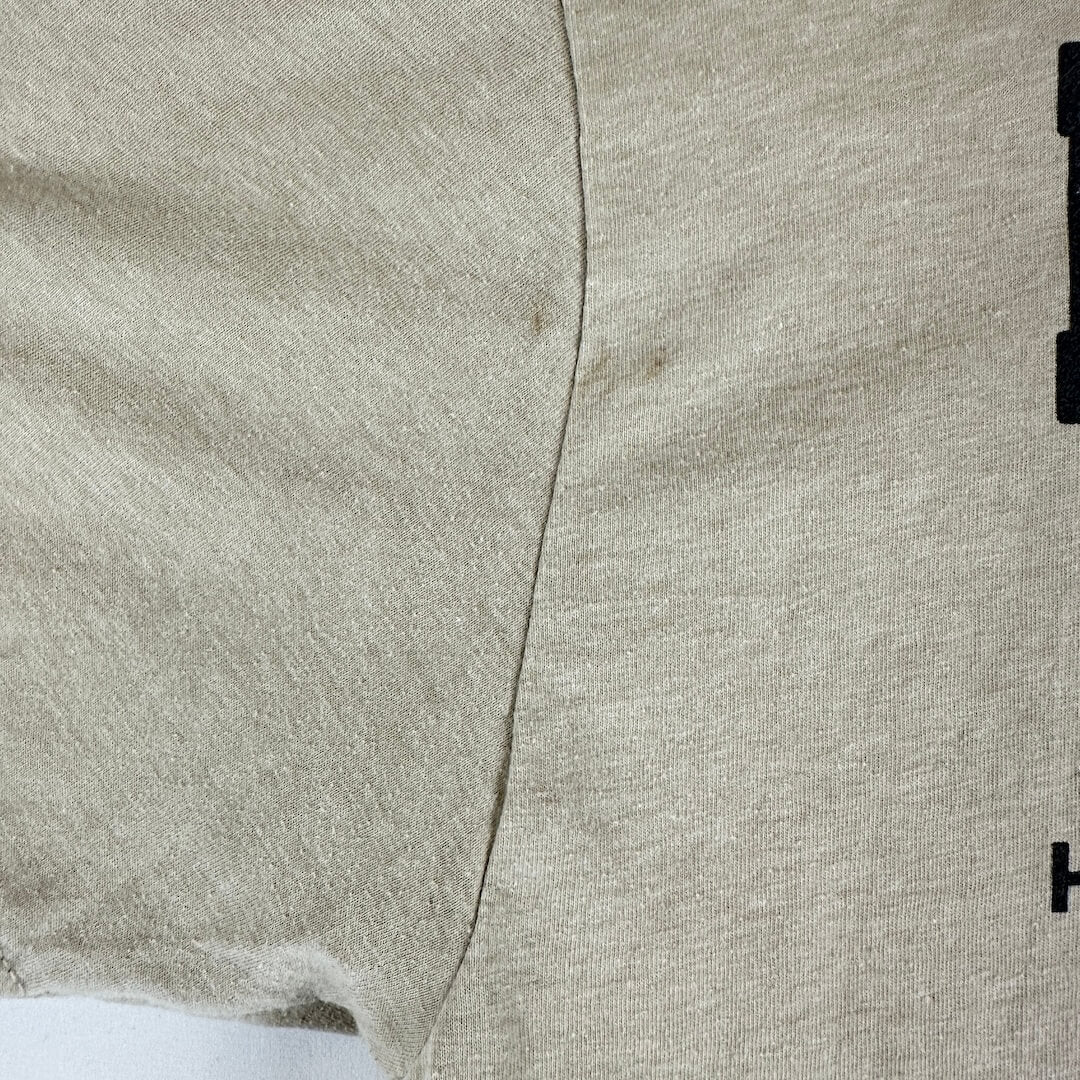 Close-up of a light beige heathered fabric with a visible center seam and a small black printed detail on the right edge.