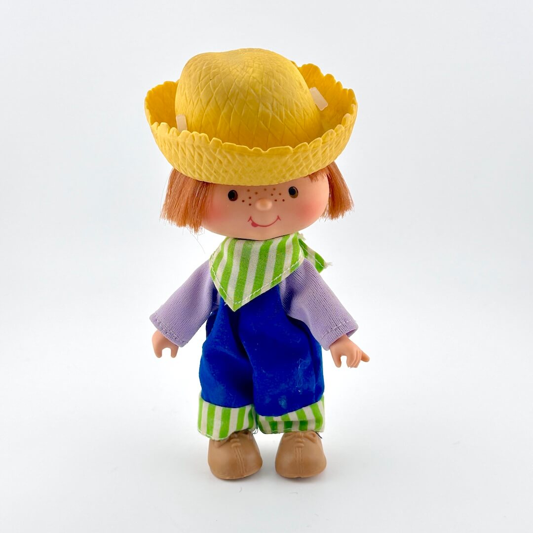Toy figure with a yellow hat, purple shirt, blue pants, and green striped scarf on a white background