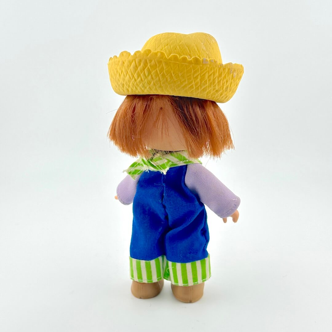 Toy figure with a yellow hat, blue overalls, and striped green and white pants on a white background