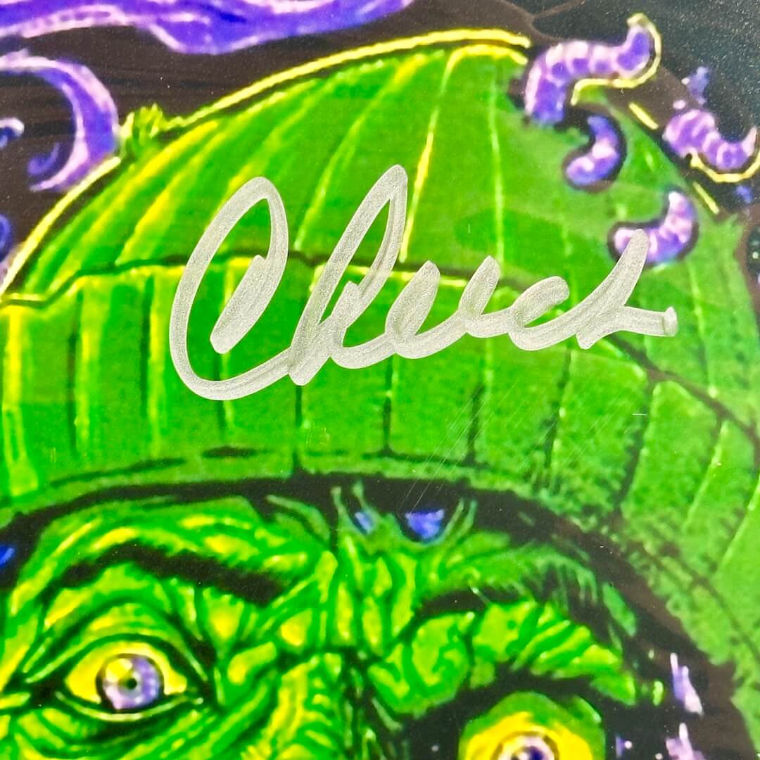 Close-up of a green creature with a hat and 'Cheech' signature in silver marker across hat.