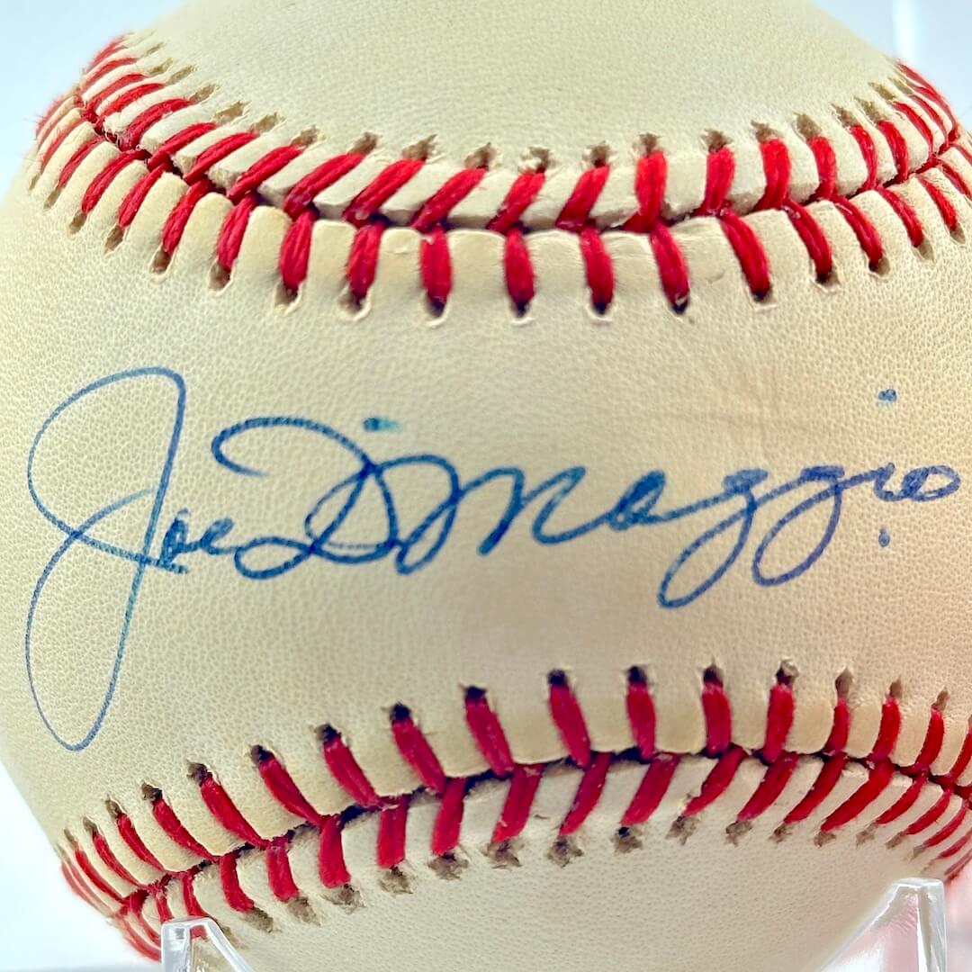 Baseball with red stitching and blue signature on a white background