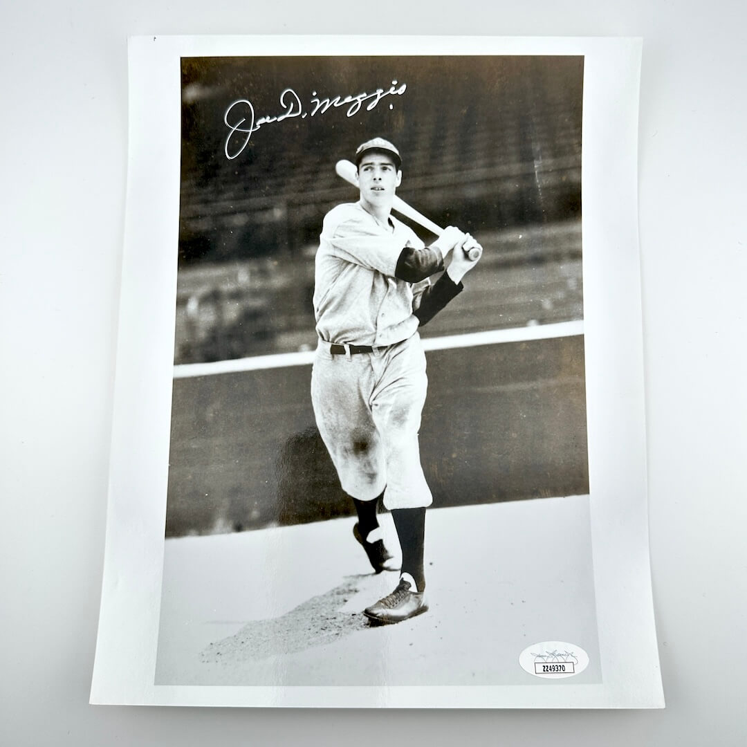 Black and white photo of a baseball player holding a bat, signed by Joe DiMaggio, on a white background.