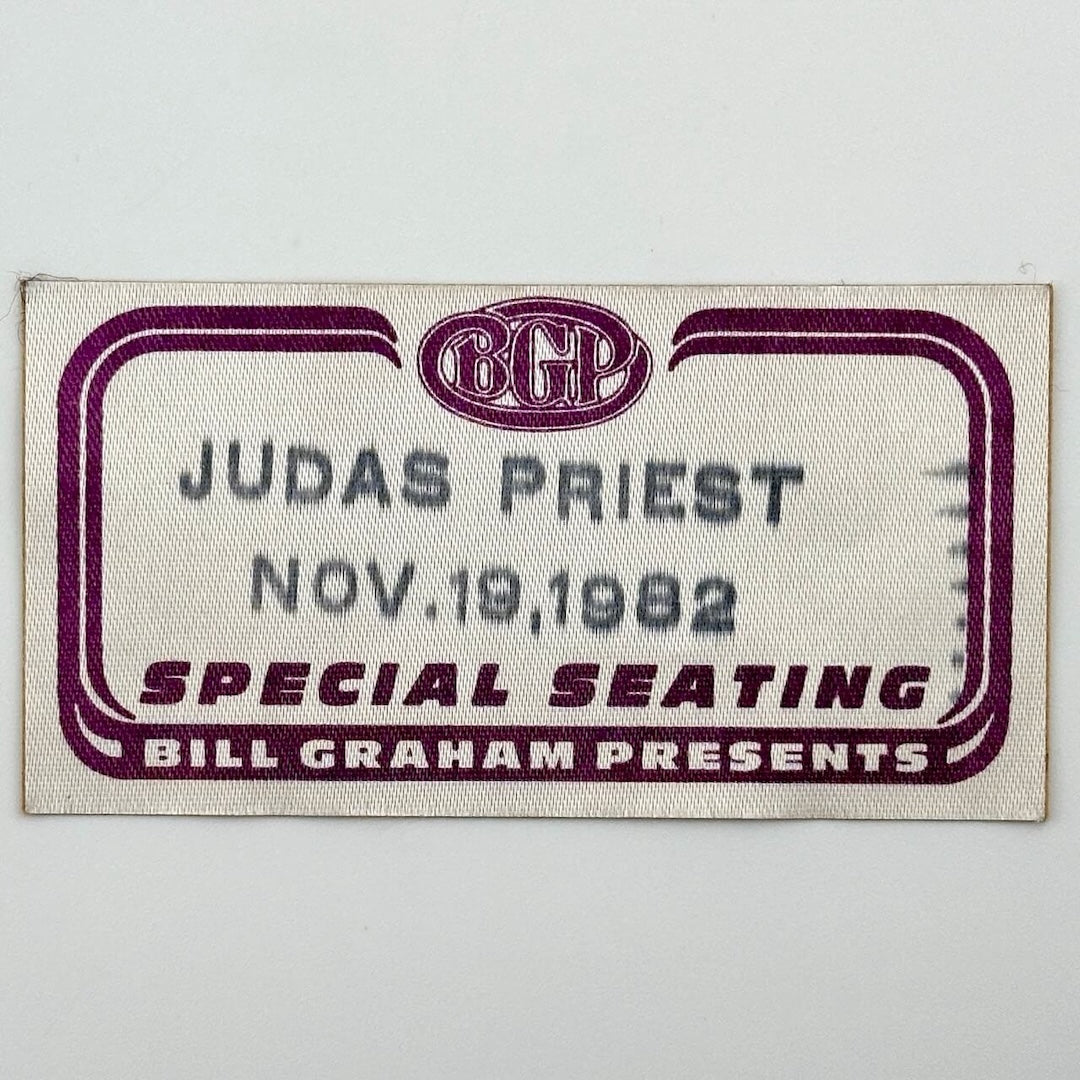 White rectangular fabric backstage pass with maroon line border, and black stamp with artist  event date.