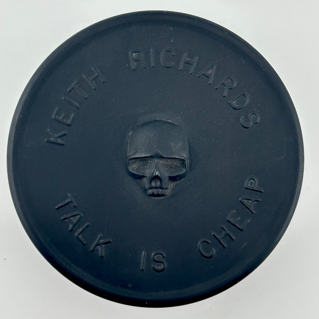 Black circular tin with "Keith Richards, Talk is Cheap" around skull in relief.