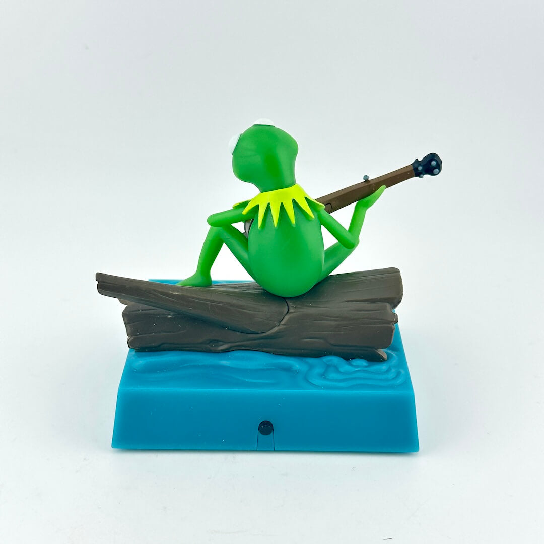 Green frog figurine playing a guitar on a blue base with wavy design