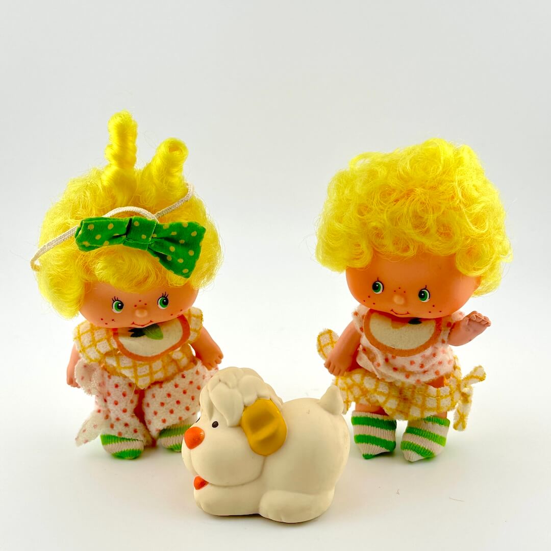 Two vintage dolls with yellow hair and a white toy dog on a light gray background