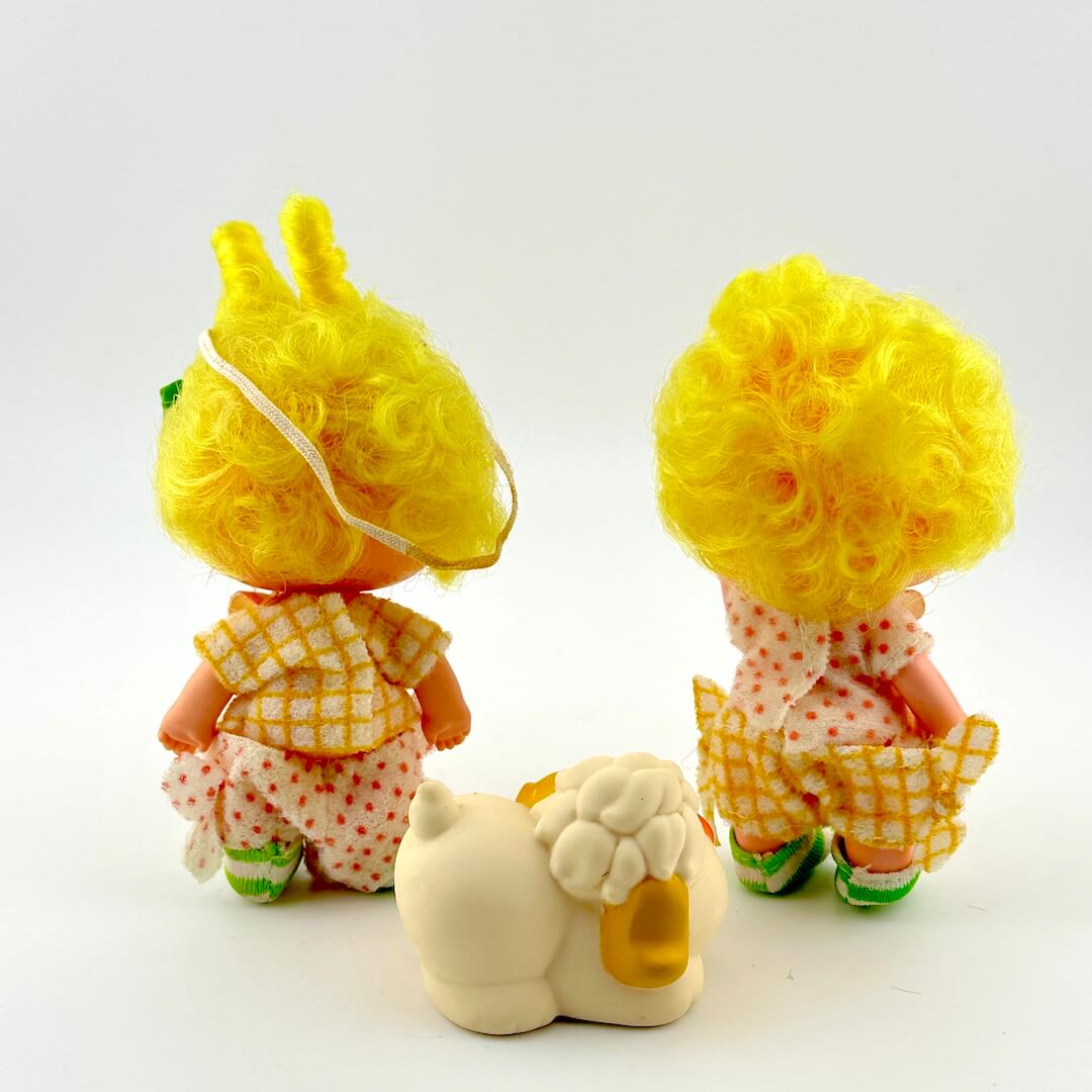 Two small dolls with yellow hair and a white dog on a light gray background