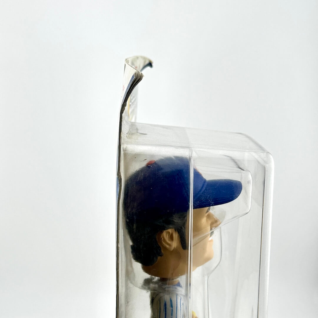 Figurine wearing a blue cap inside a clear plastic box on a white background