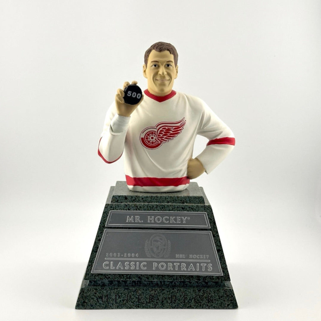 Man holding "500" puck in white Red Wings Jersey atop marble looking pedestal with silver plaque.