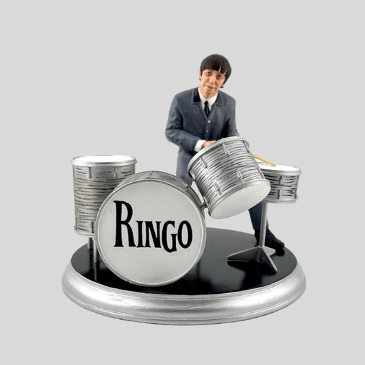 Figurine of Ringo Starr sitting at silver drum set on silver and black base.