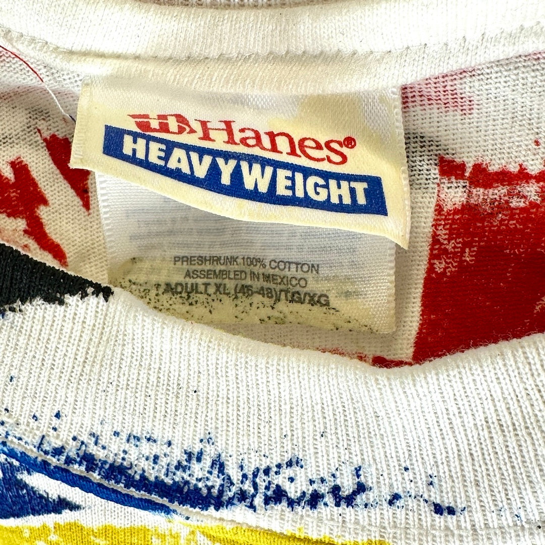Close-up of XL Hanes Heavyweight t-shirt tag, showing 'preshrunk 100% cotton' and 'assembled in Mexico,' with red, blue, yellow design details.