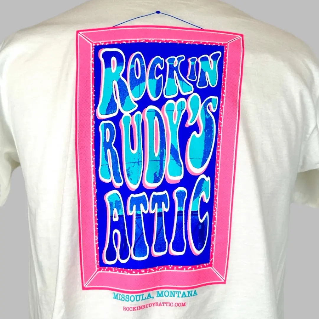 White short sleeve t-shirt with pink art frame with Rockin Rudy's Attic in center with Peace Sign sign in text.