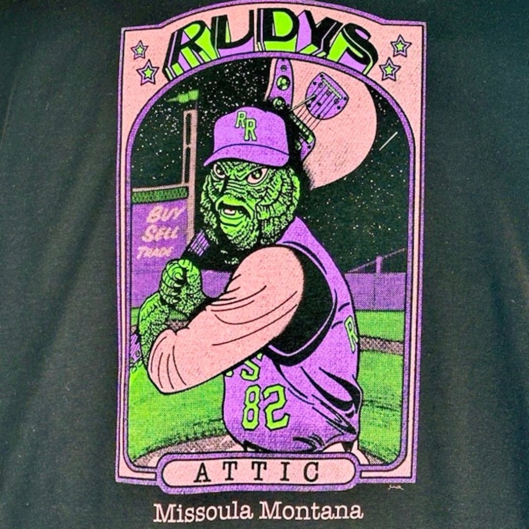 Back graphic of baseball card style logo with Swamp Thing swinging a guitar. Rudy's at top, Attic at base above Missoula, MT.