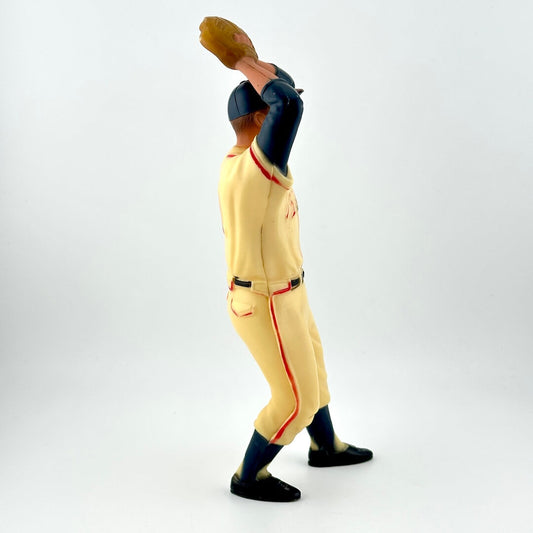 Figurine of baseball player in Braves uniform in mid-wind up to pitch, so arms raised with hands & glove over head.