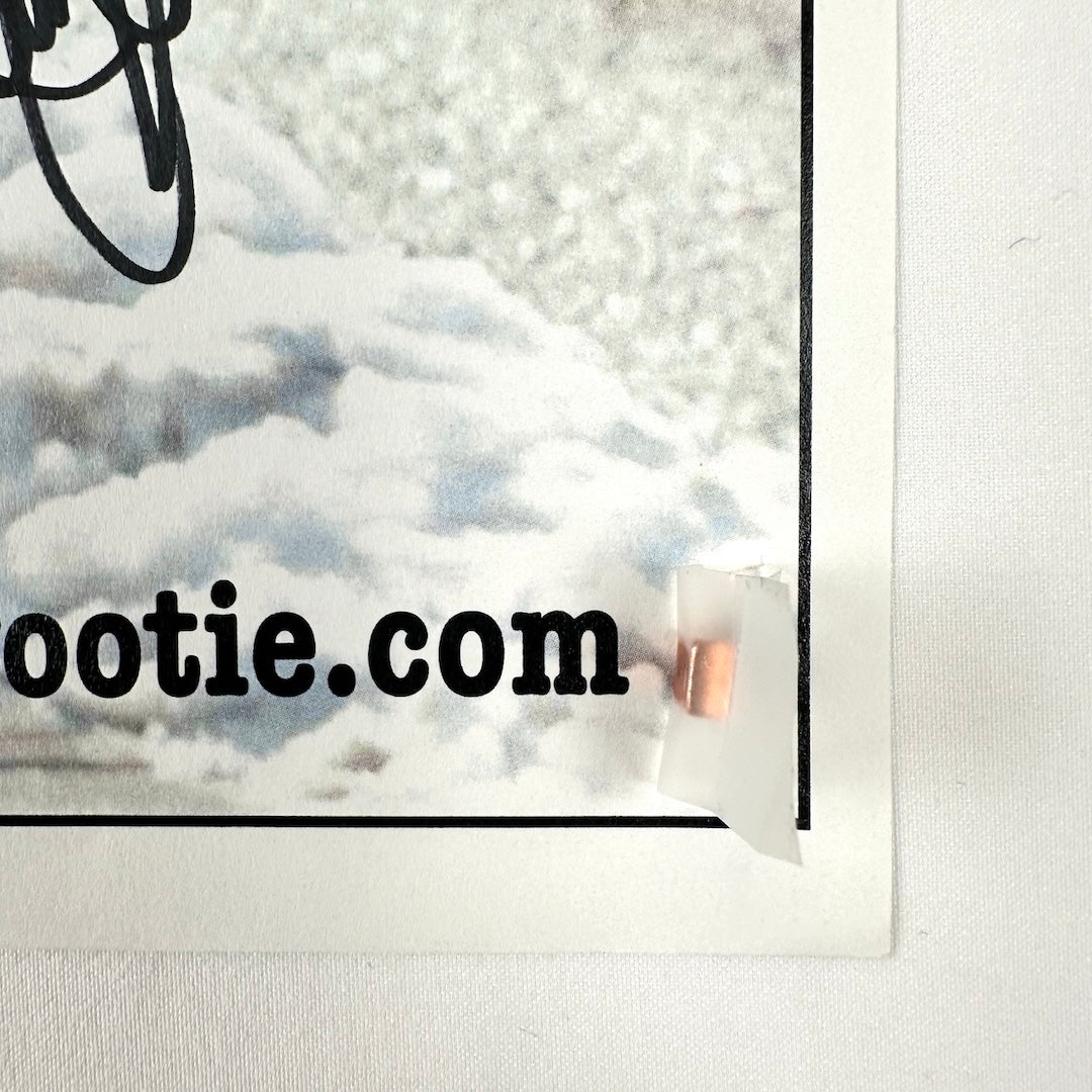 Bottom right corner showing no damage to corner or edges, snow covered ground seen in background & partial signature.